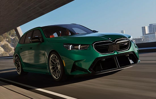 Green BMW M5 Touring driving on a city road. | Tom Bush BMW Orange Park in Jacksonville FL